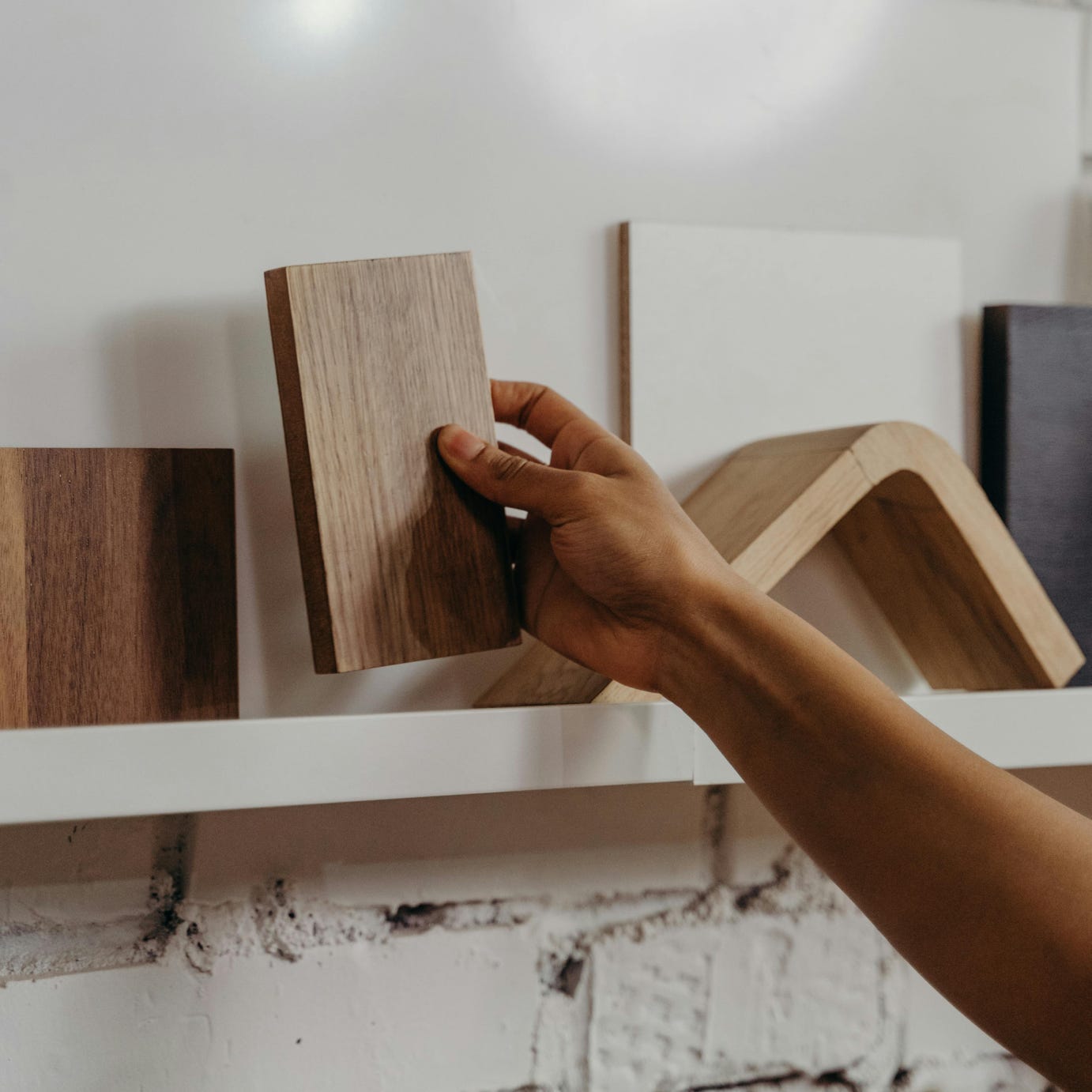 A hand picks up a wooden sample from a shelf with various design elements, highlighting interior choices.