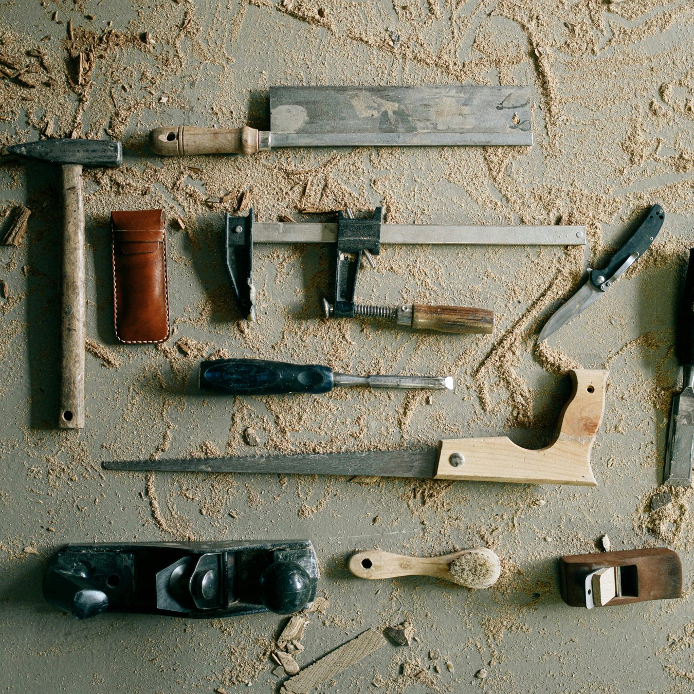 A collection of vintage woodworking tools on a sandy workbench, evoking a rustic and crafted feel.